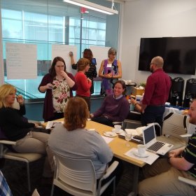 Participants are grouped around a table, discussing and recording their ideas.