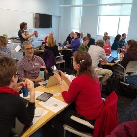 A classroom with faculty grouped around tables, sharing ideas.