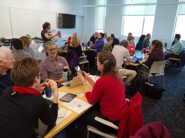 A classroom with faculty grouped around tables, sharing ideas.